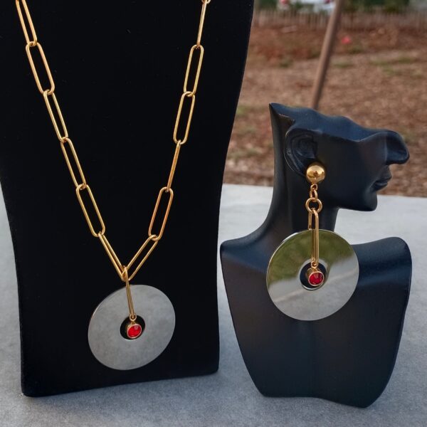 Parure 2 Pièces AMINA Un bijou fait main associant chaînes en mailles Trombones dorées, un pendentif disque en acier argenté et une breloque en strass de cristal rouge. Parfait pour toutes les occasions, apportant élégance et prestige.